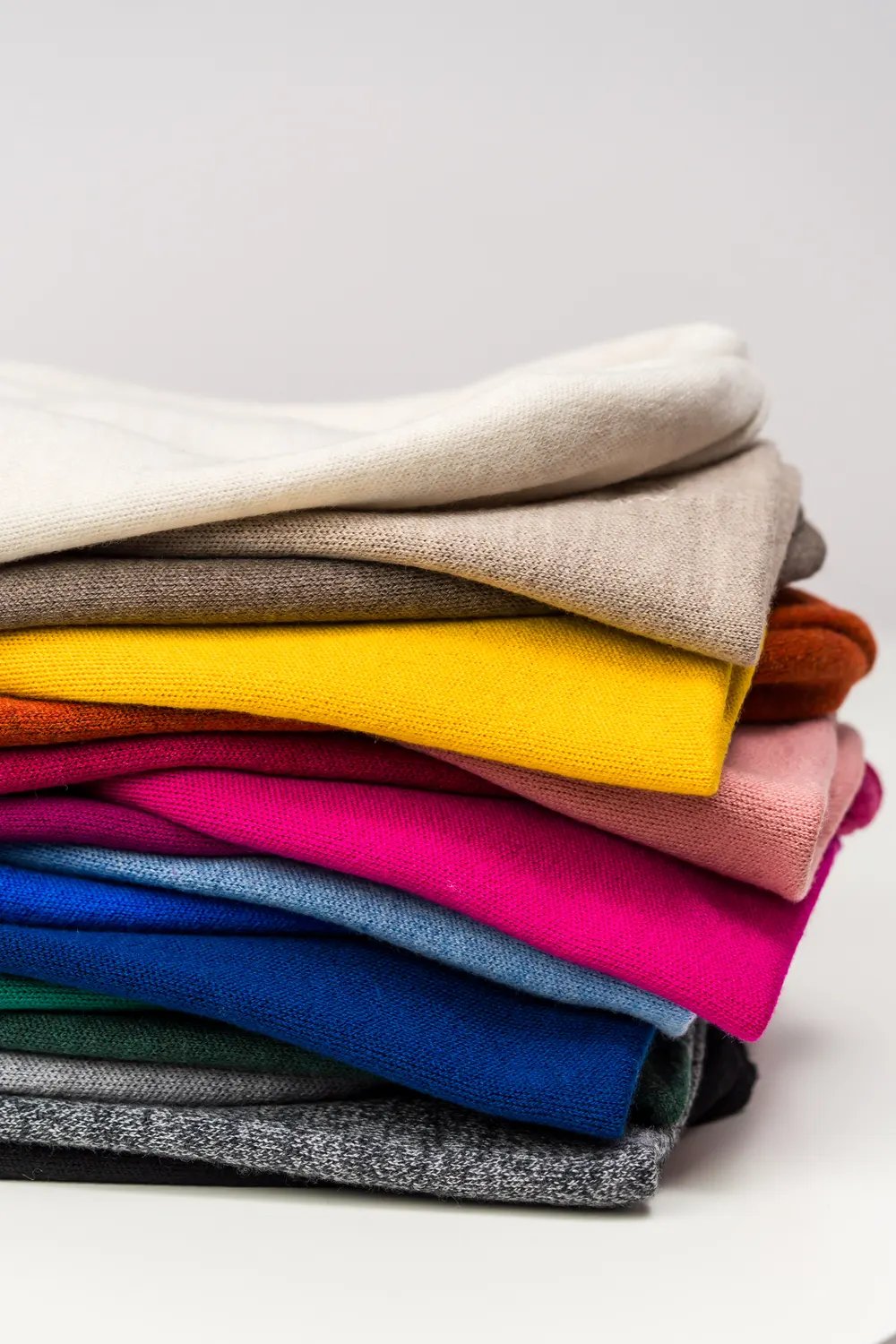 Stack of knits in the full yarn-card palette — from white and beige to fuchsia and cobalt