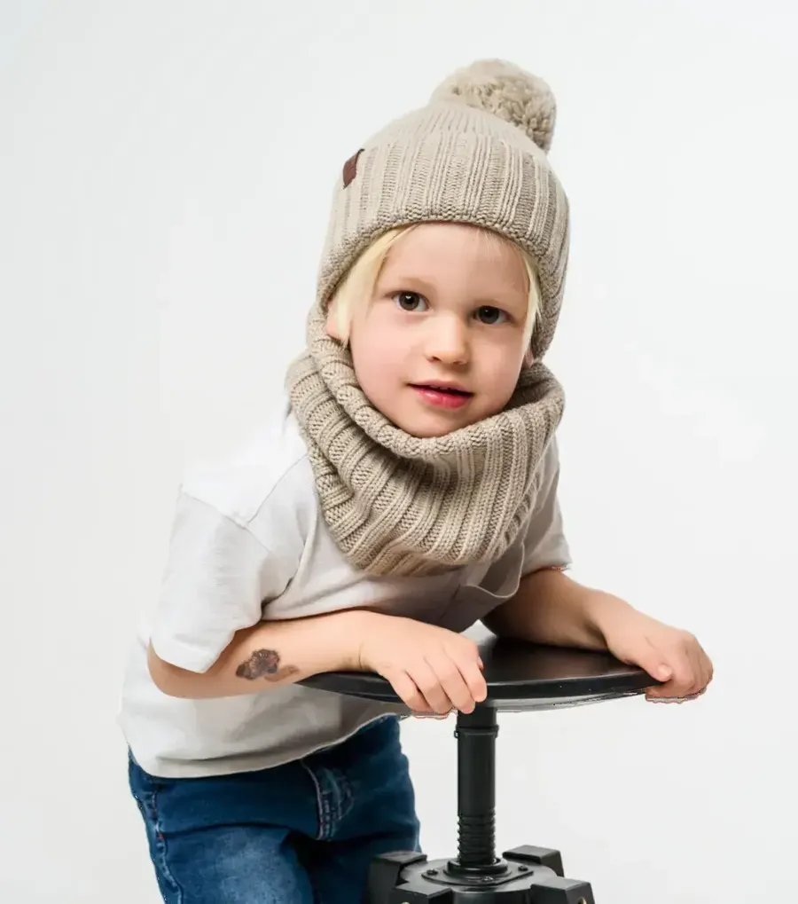 Child in a beige pom-pom beanie and knitted neck warmer